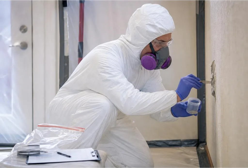 Asbestos testing technician in protective equipment collecting a controlled building-material sample